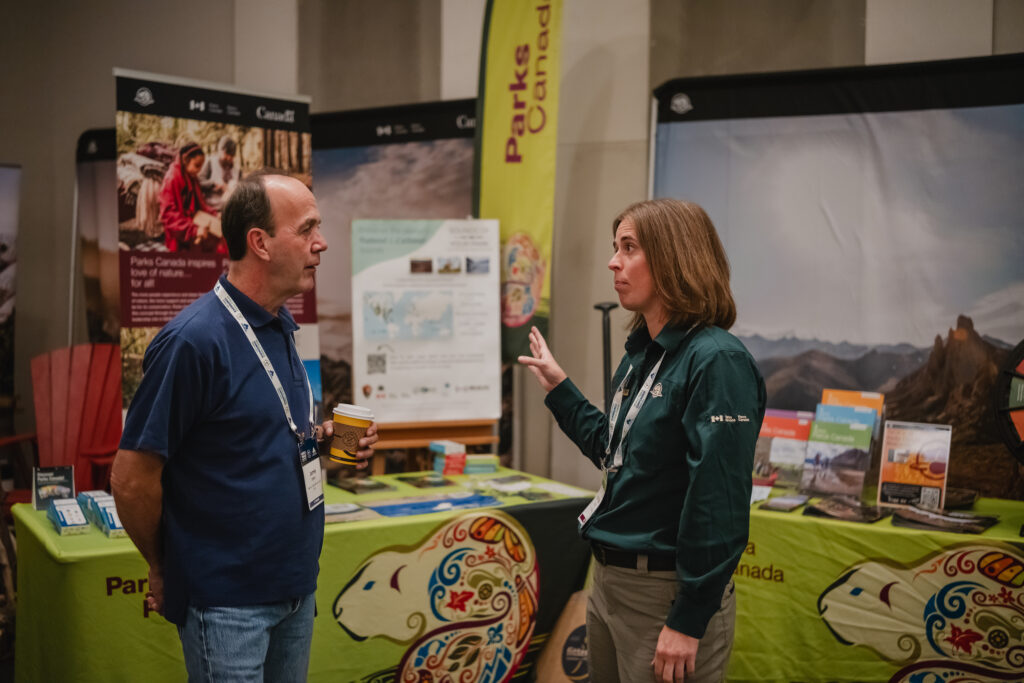 Two people talk in front of a Parks Canada display in a conference room.